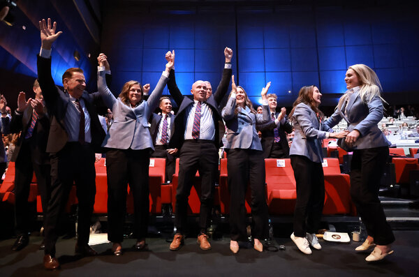 A group of people in business attire smiling with their hands raised. Some are jumping with excitement.