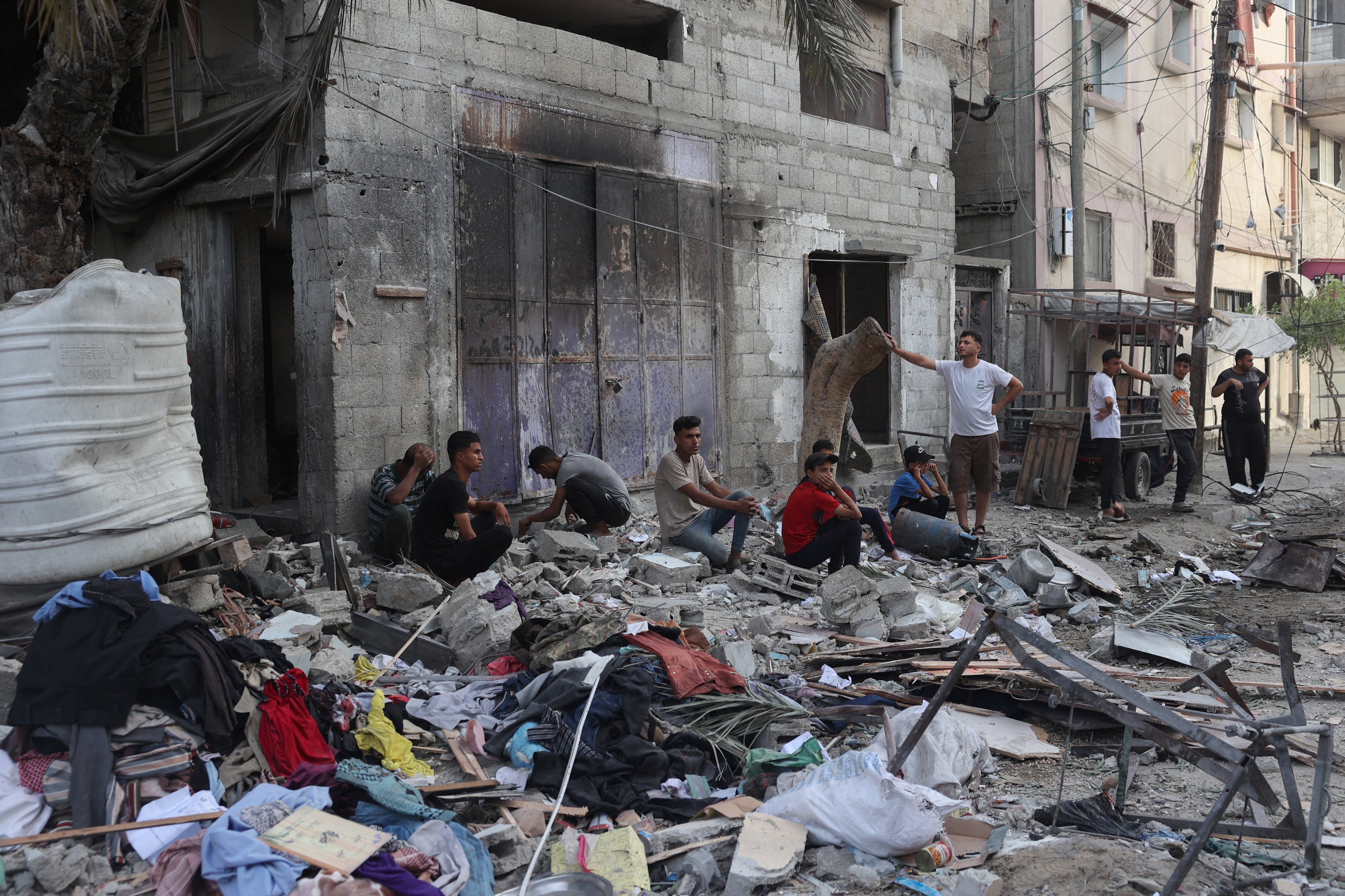 Palestinians sit by the debris of a household home that was struck overnight in Israeli barrage in the Tal al-Sultan area of Rafah in southern Gaza