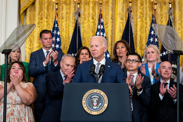 President Biden stands at a lectern, as people behind him applaud.