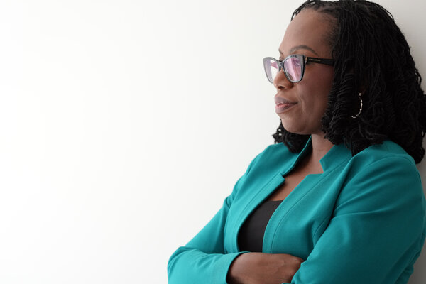 A portrait of Justice Ketanji Brown Jackson wearing a teal jacket, black shirt, and black glasses.